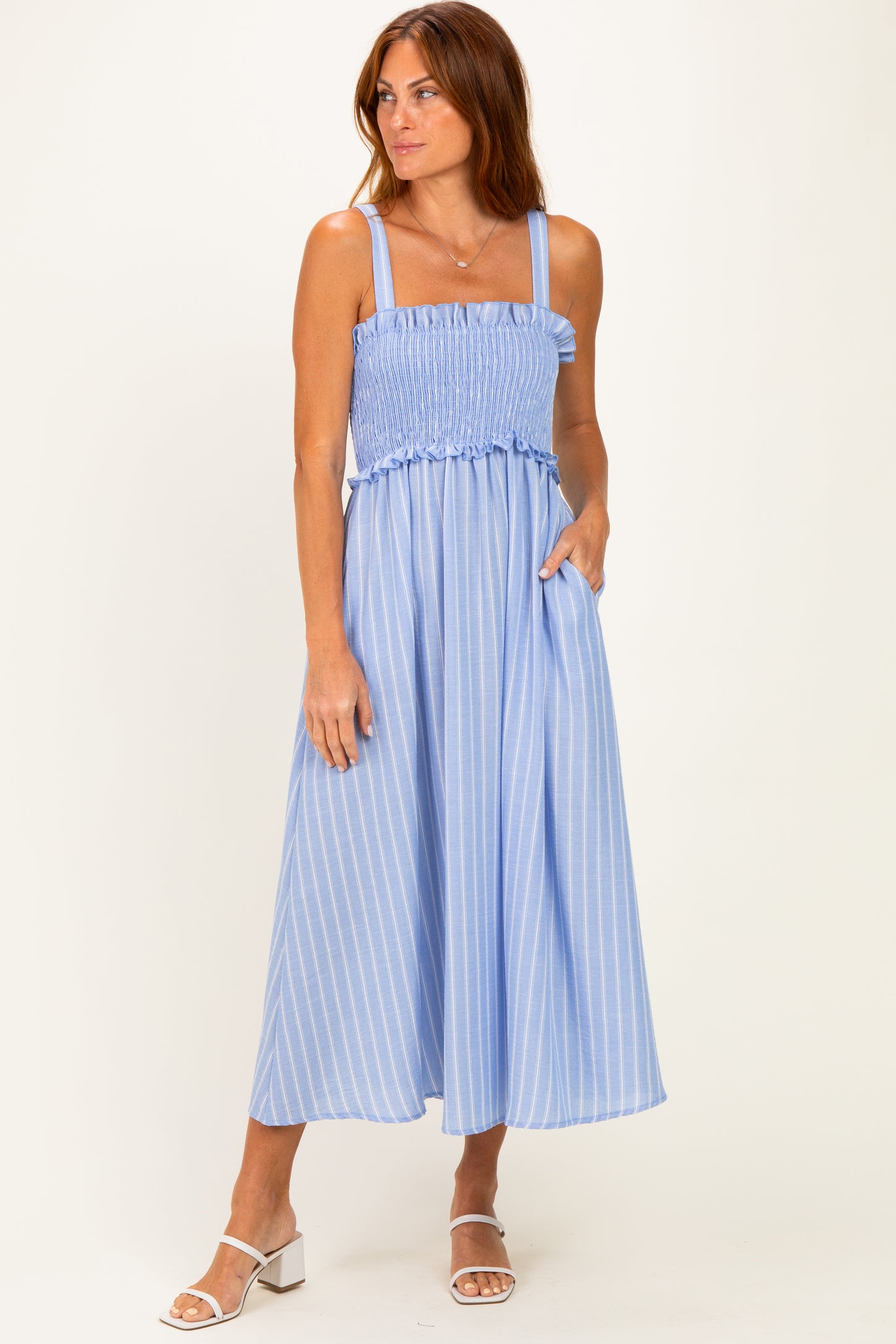 woman wearing a light blue striped midi dress with smocked bodice and pockets, standing on a beige background