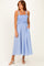 woman wearing a light blue striped midi dress with smocked bodice and pockets, standing on a beige background