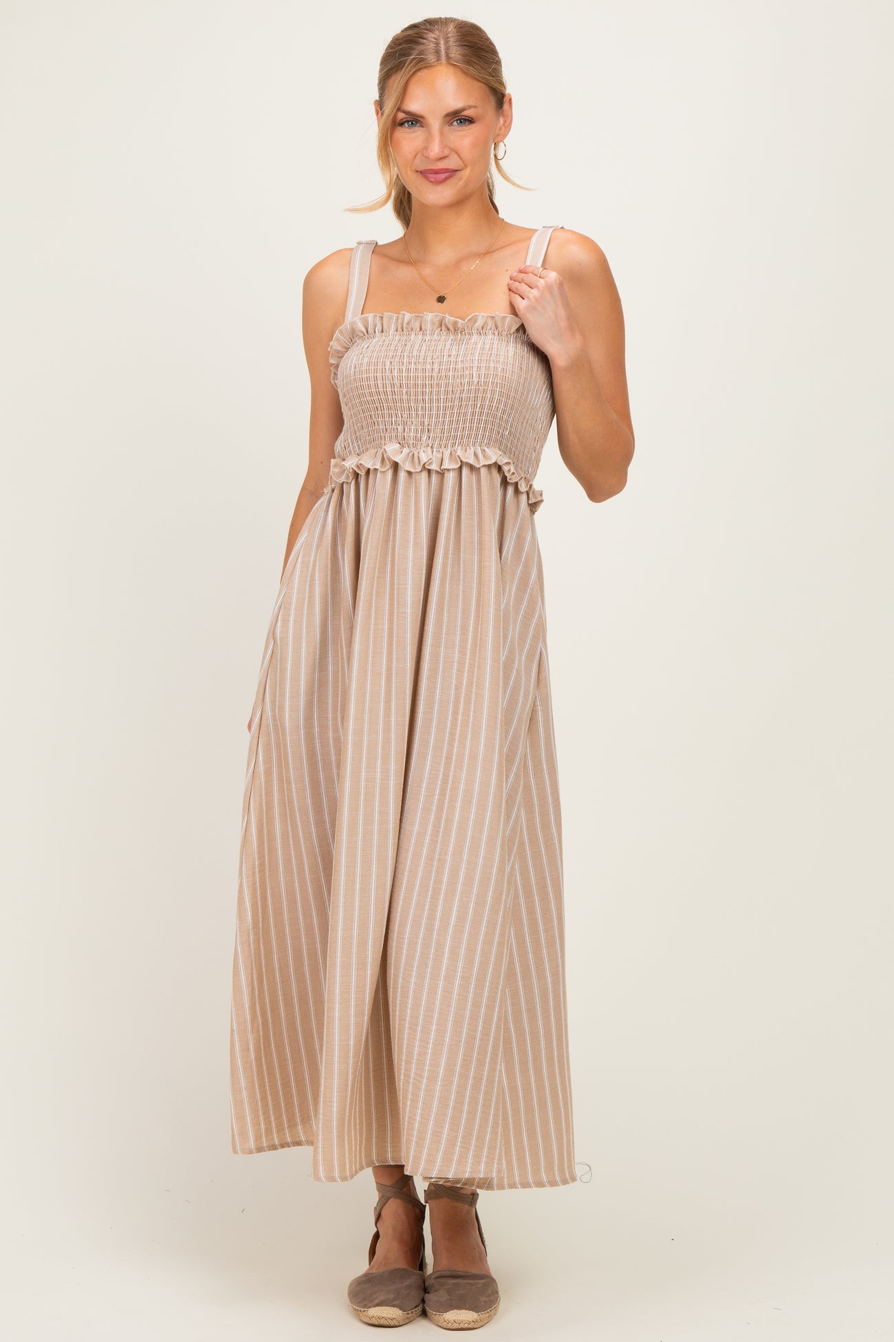 woman wearing a beige striped maxi dress with a smocked bodice and ruffle detail, smiling at the camera