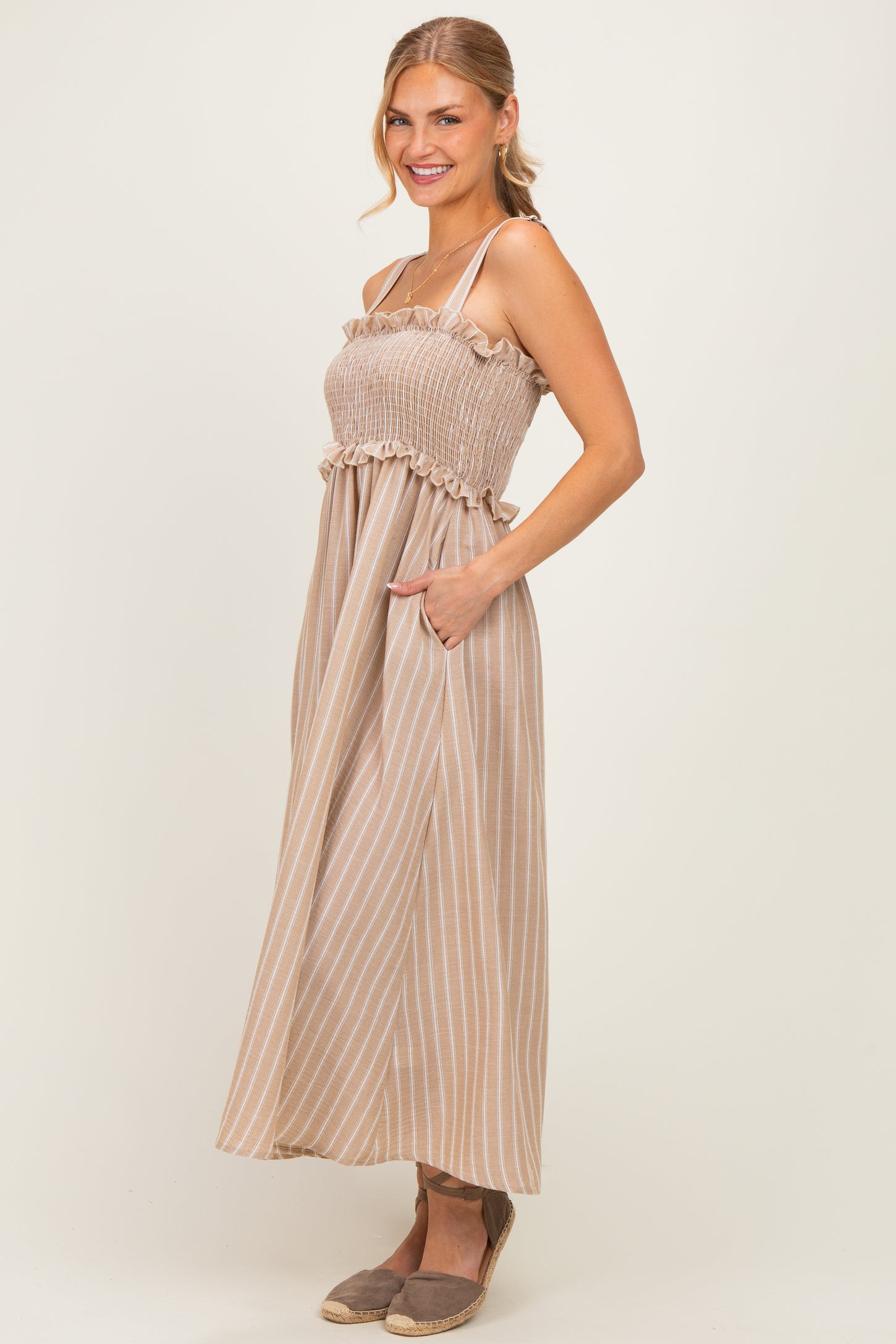 woman wearing a beige and white striped maxi dress with a smocked bodice and ruffled straps, posing with hands in pockets