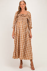 woman wearing a brown and beige checkered maternity maxi dress with puff sleeves and a ruffled neckline, showing her baby bump