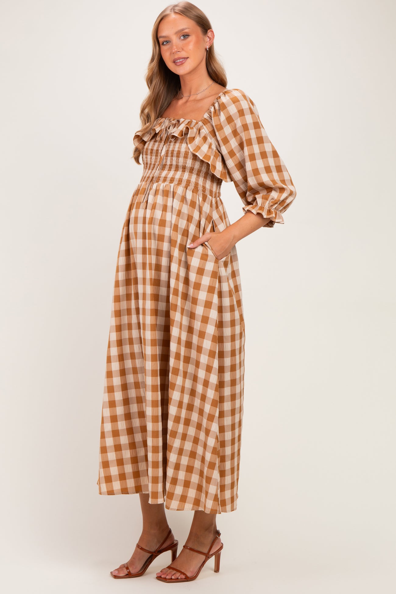 woman wearing a brown and cream gingham maternity maxi dress with ruffled neckline and pockets, showing her baby bump