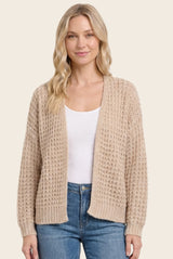 woman wearing a beige knitted cardigan over a white top and blue jeans