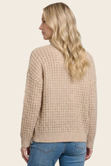 woman wearing a cozy beige knit sweater with a textured pattern, viewed from the back, paired with light blue jeans
