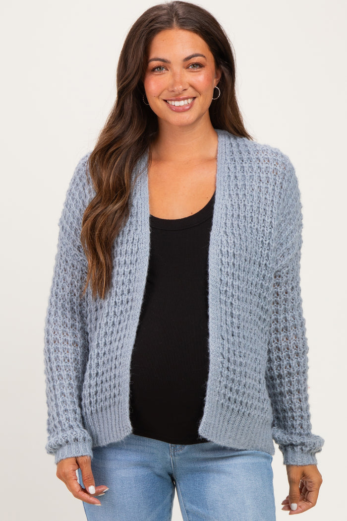 woman wearing a light blue maternity cardigan over a black top, showing her baby bump with a relaxed smile