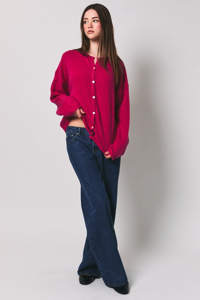 woman wearing a fuchsia oversized cardigan with button details and wide-leg jeans