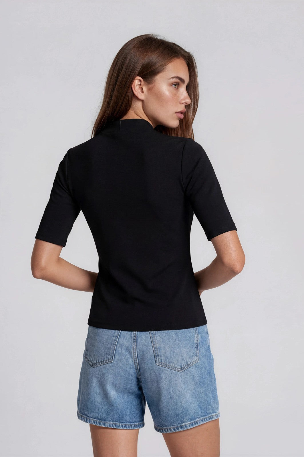 woman wearing a fitted black short sleeve top and light blue denim shorts, viewed from the back