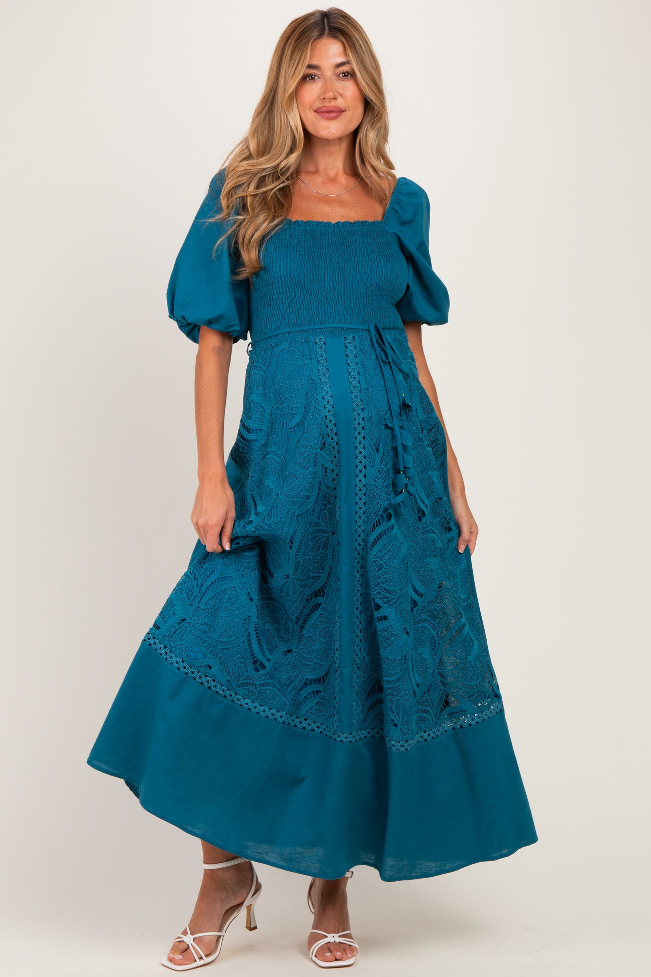 woman wearing a teal maternity maxi dress with puff sleeves and lace detailing, showcasing her baby bump