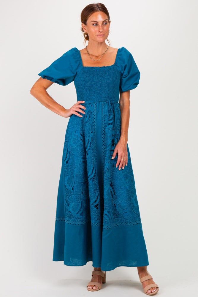 woman wearing a teal square neck maxi dress with puff sleeves and embroidered details, standing against a white background