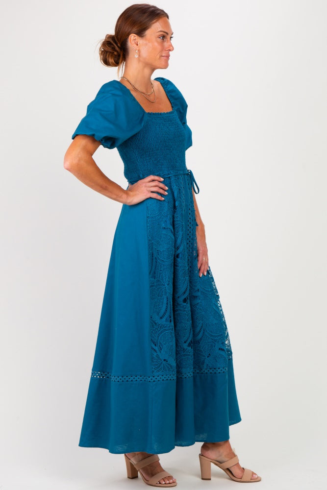 woman wearing a teal maxi dress with puff sleeves and lace detailing, standing in profile