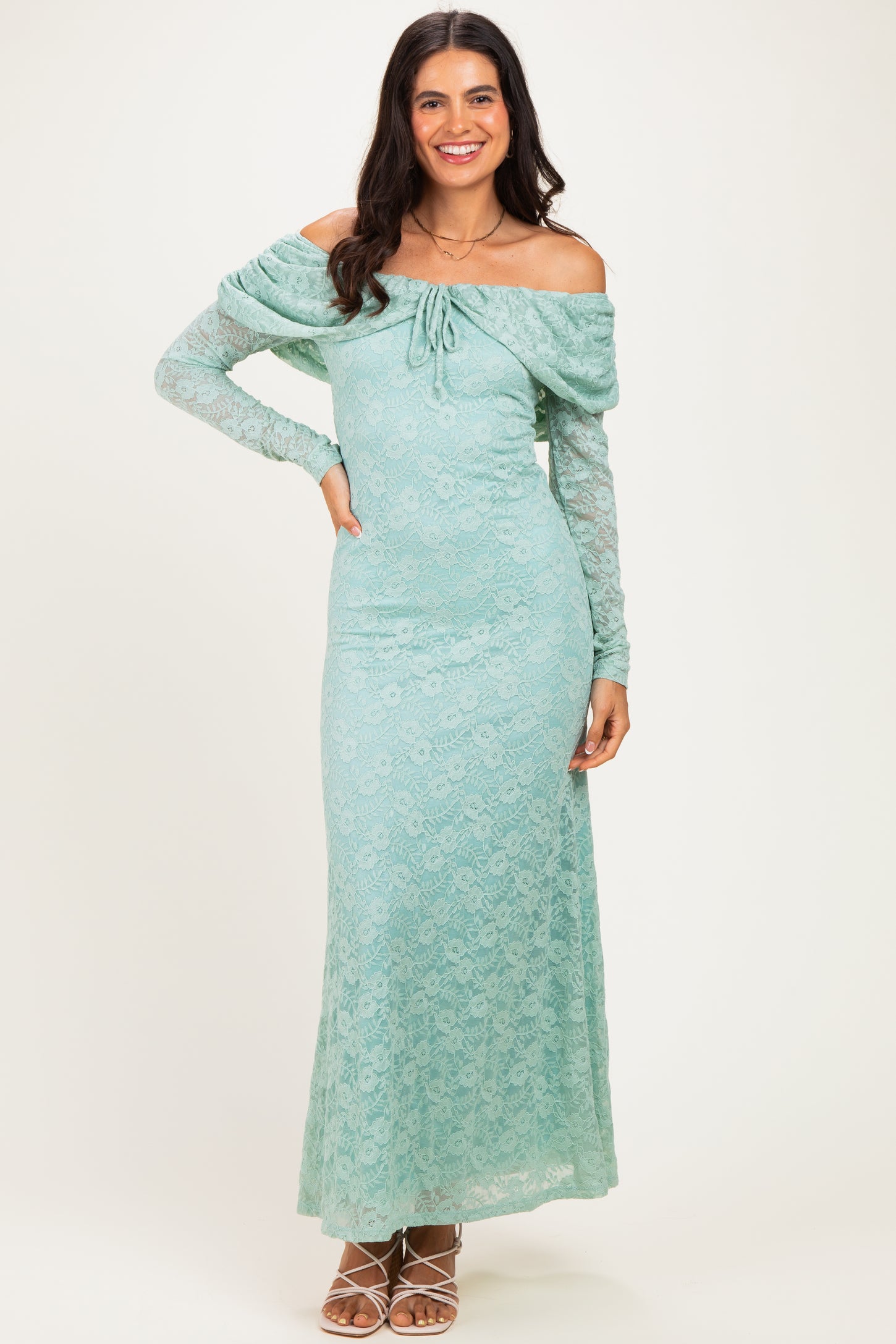 woman wearing a light teal off-the-shoulder lace maxi dress with long sleeves and a drawstring detail