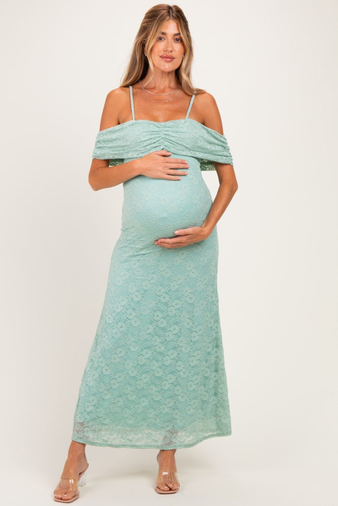 woman wearing a mint green off-shoulder lace maternity dress and cradling her baby bump