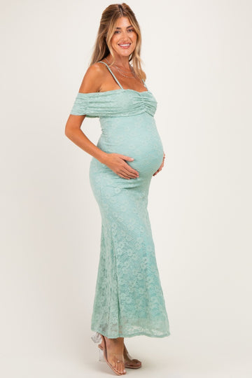 woman wearing a light teal off-the-shoulder lace maternity dress and holding her baby bump