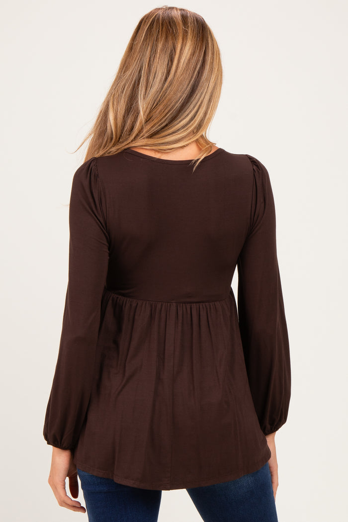woman wearing a dark brown maternity top with a gathered waist and long bell sleeves, showing a baby bump