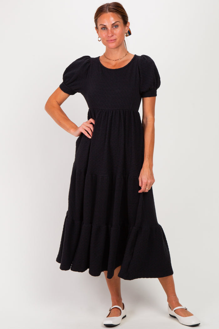 woman wearing a black puff sleeve midi dress with tiered ruffles and a round neckline