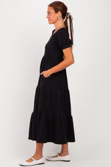 woman wearing a black tiered maxi dress with puff sleeves and pockets, styled with a hair ribbon and white flats