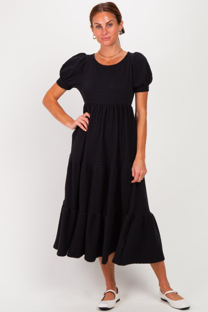 woman wearing a black puff sleeve midi dress with tiered ruffles and a round neckline