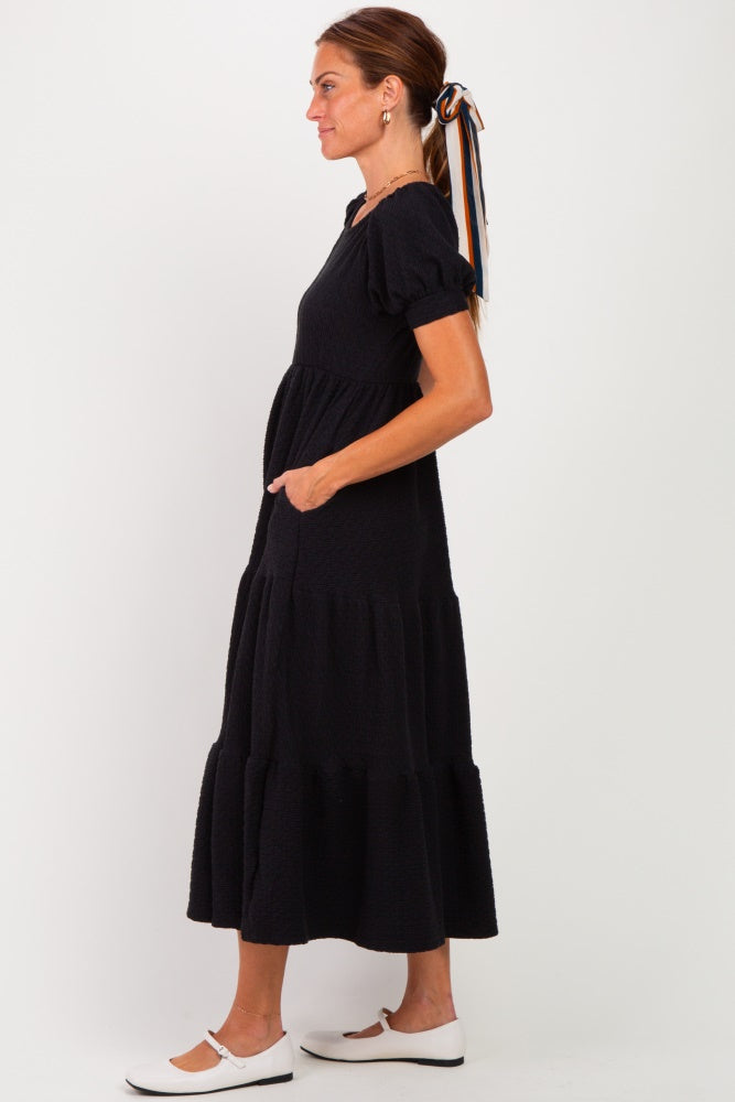 woman wearing a black tiered maxi dress with puff sleeves and pockets, styled with a hair ribbon and white flats