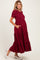 woman wearing a burgundy maternity maxi dress with puff sleeves and side pockets, showing her baby bump