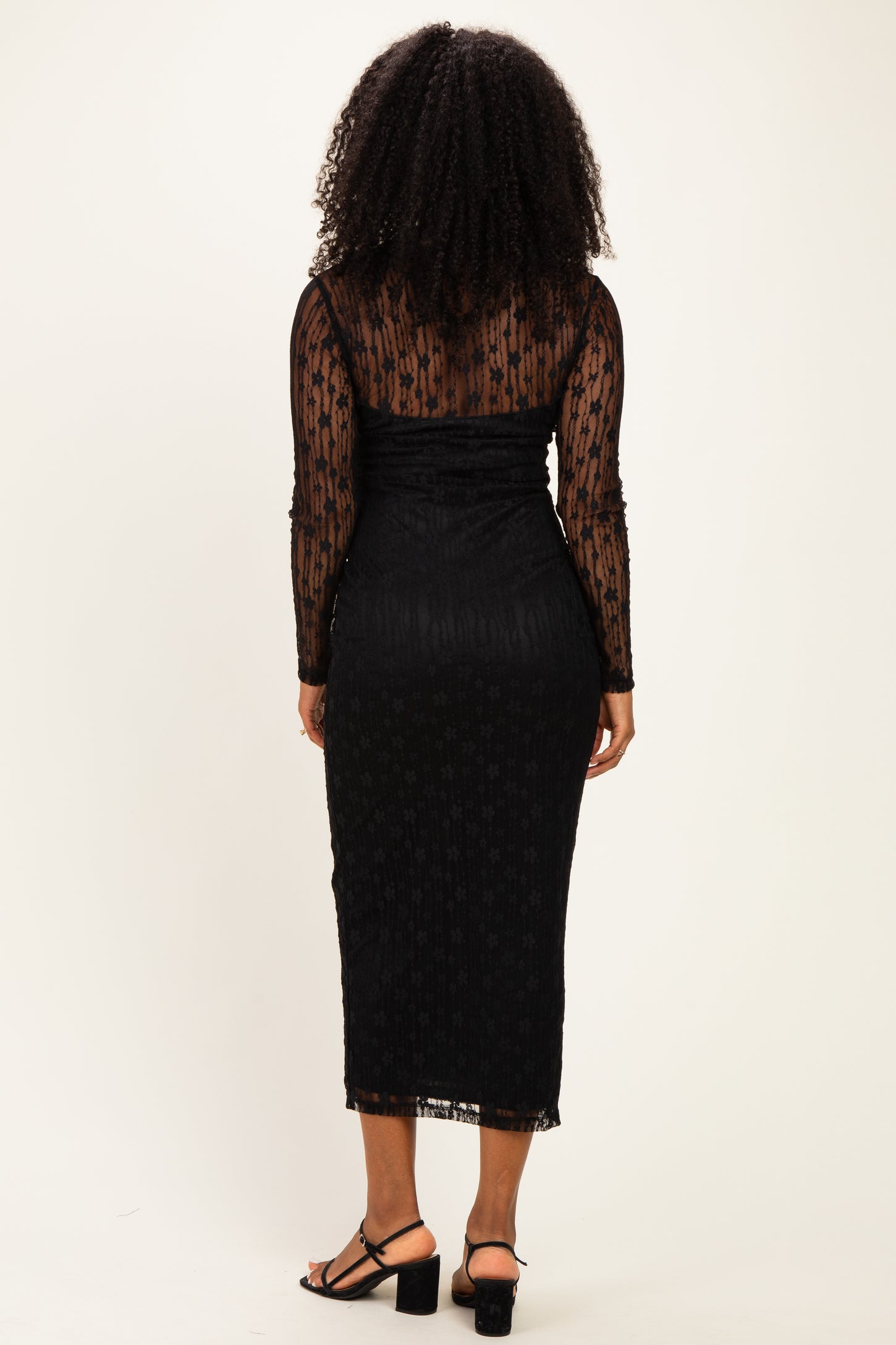 woman wearing a black long sleeve midi dress with sheer floral details and ruched back, standing with back to the camera