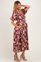 woman wearing a burgundy floral print maternity dress with puff sleeves and pockets, showcasing her baby bump