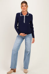 woman wearing a navy blue maternity top with a white collared neckline and stylish buttons, holding her baby bump, paired with light blue jeans