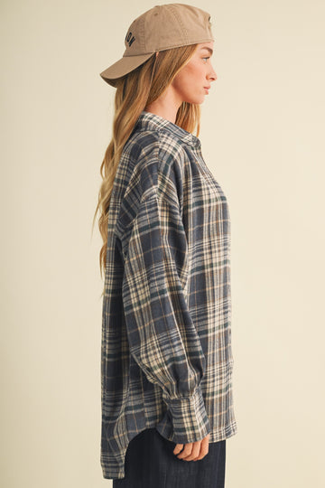 woman wearing a navy and beige plaid oversized shirt with long sleeves and a beige baseball cap