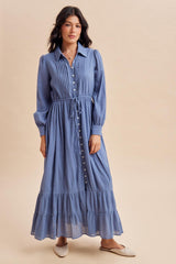 woman wearing a long sleeve light blue button-up maxi dress with a tiered skirt and tie waist detail