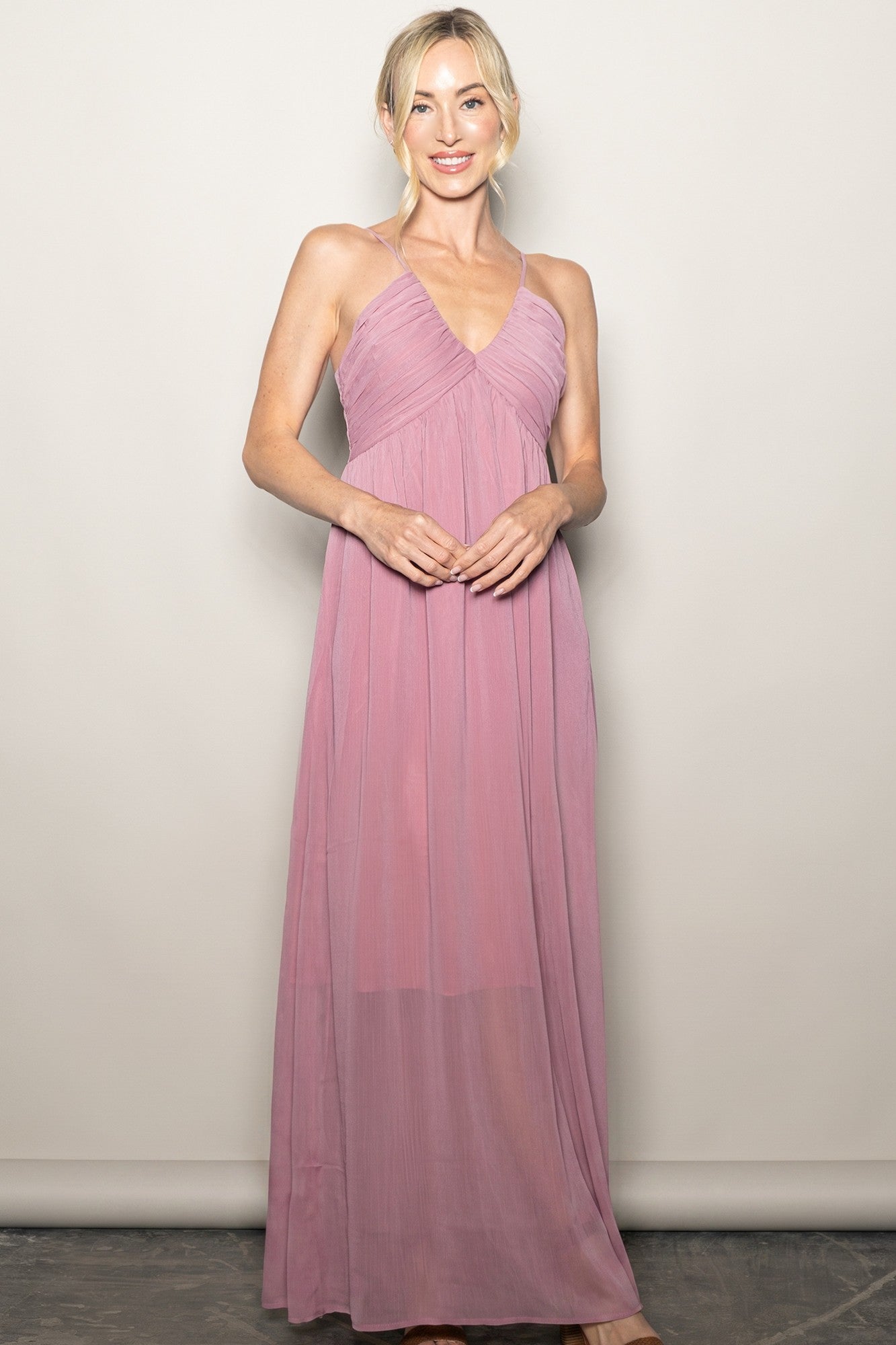 woman wearing a light pink halter maxi dress with a gathered bodice and flowing skirt