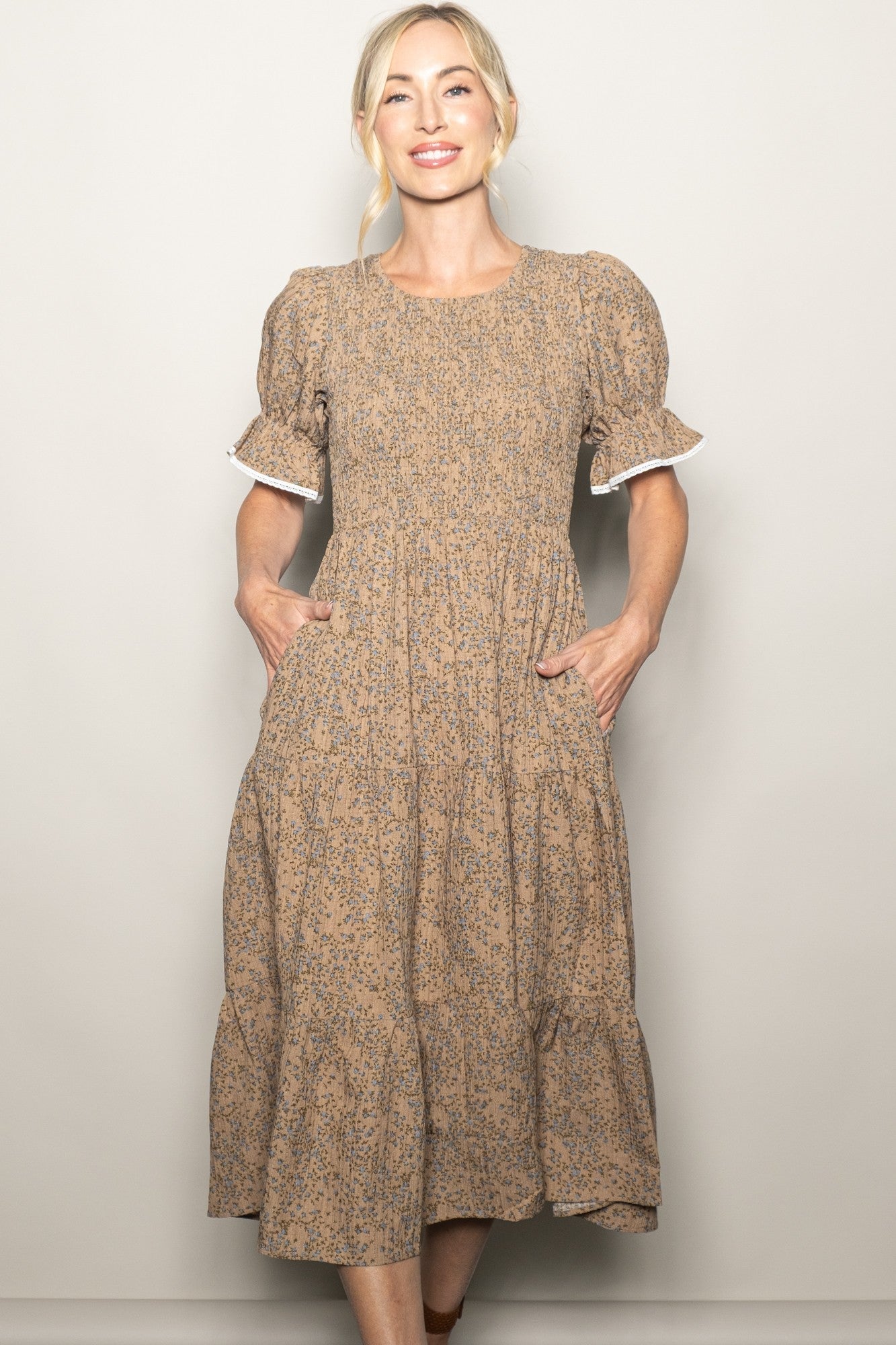 woman wearing a beige floral midi dress with short puff sleeves and pockets, standing and smiling