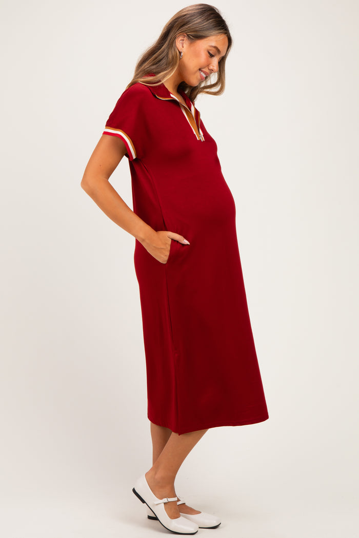 woman wearing a burgundy short sleeve maternity dress with pockets and a collar, showing her baby bump