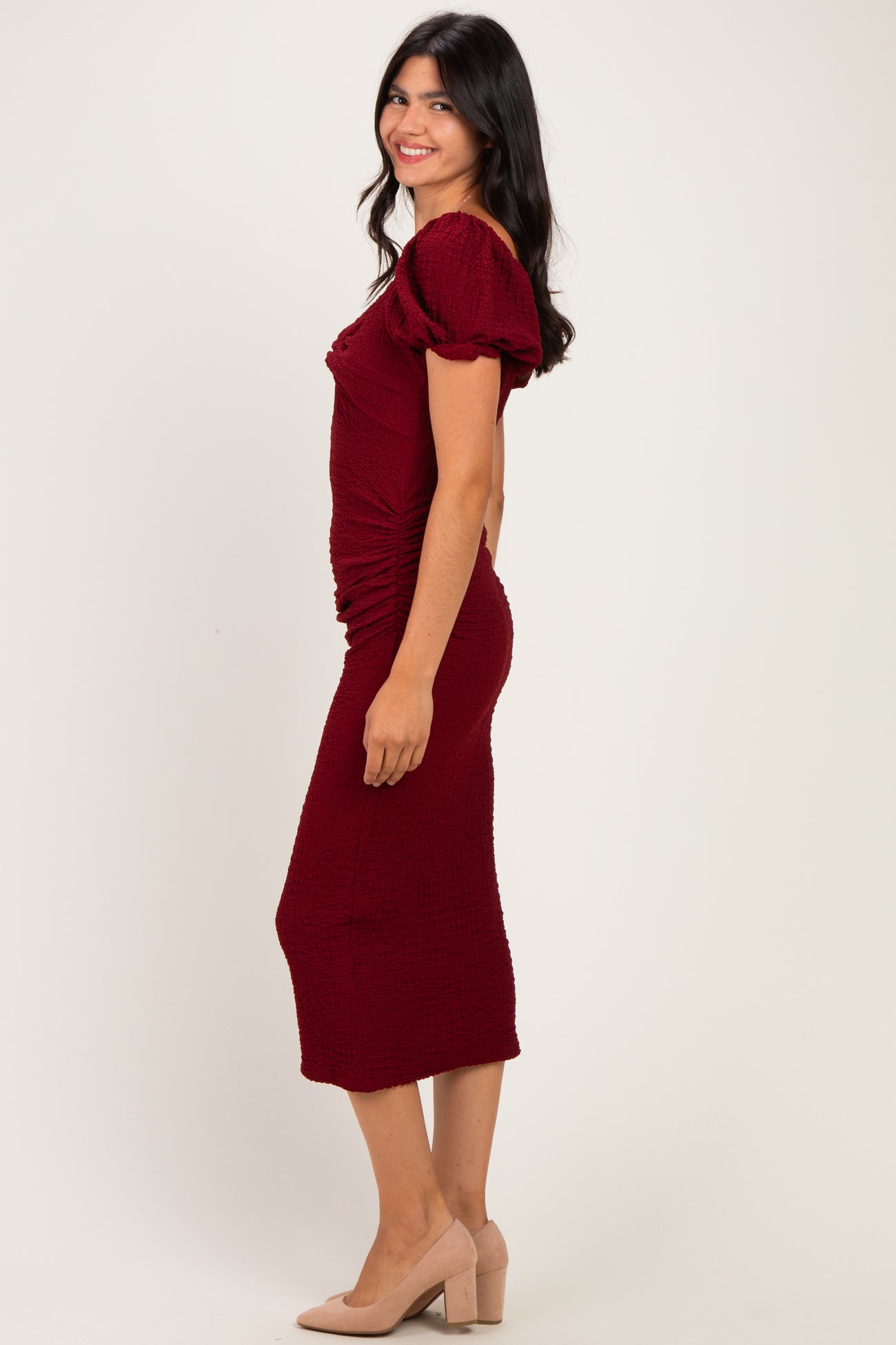 woman wearing a burgundy midi dress with puff sleeves and ruched detailing, paired with nude block heel shoes