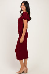 woman wearing a burgundy midi dress with puff sleeves and ruched detailing, paired with nude block heel shoes