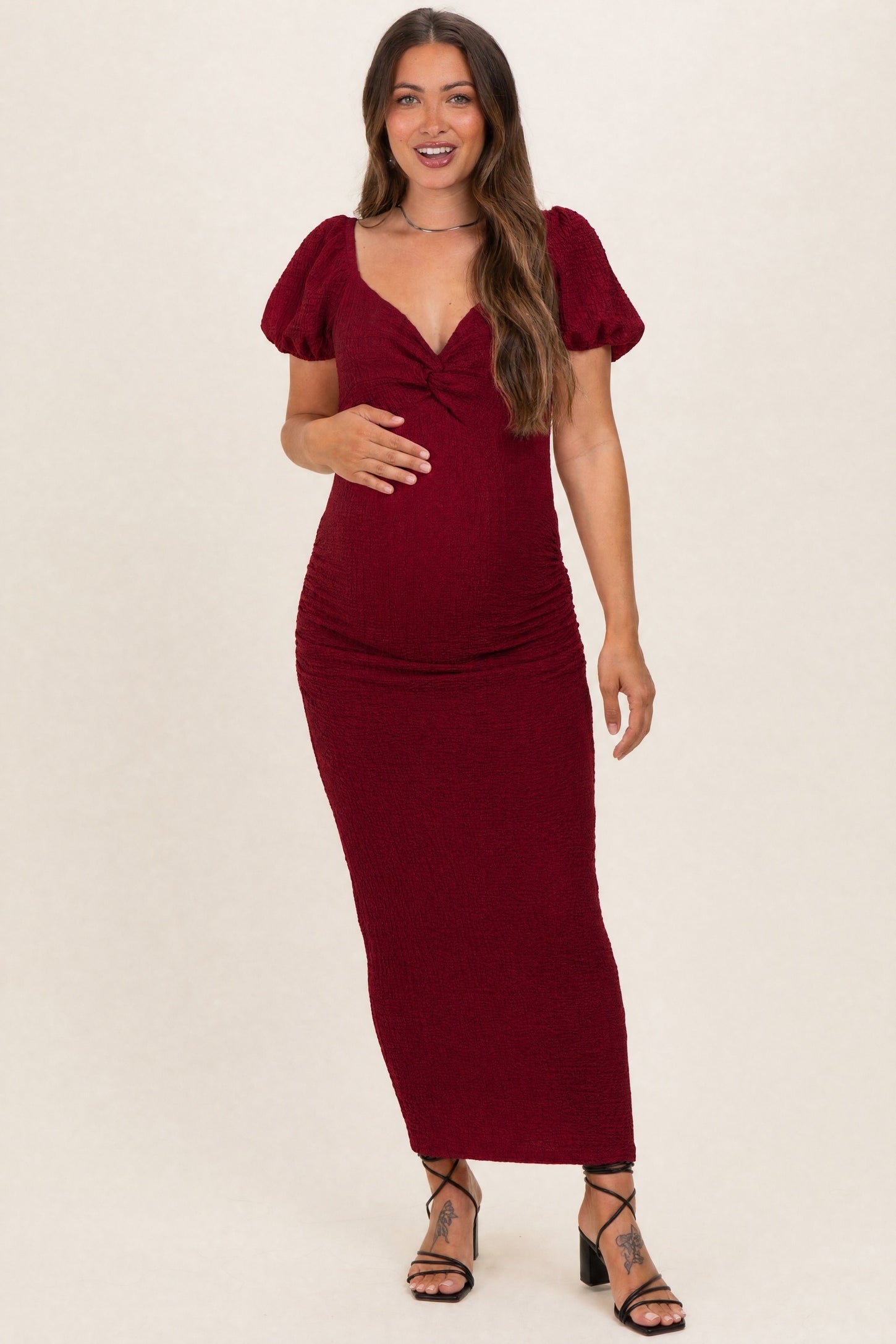 woman wearing a burgundy maternity maxi dress with puff sleeves and gathering at the waist, showing her baby bump