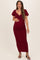 woman wearing a burgundy maternity maxi dress with puff sleeves and gathering at the waist, showing her baby bump