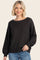 woman wearing a black ribbed sweater with a wide neckline and balloon sleeves, paired with light blue jeans