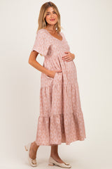 woman wearing a pink floral maternity dress with short sleeves and a tiered skirt, holding her baby bump