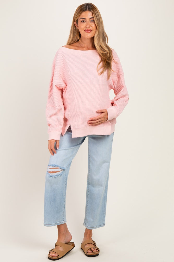 woman wearing a pink ribbed maternity sweater and holding her baby bump with light blue ripped jeans