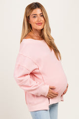 woman wearing a light pink oversized maternity sweater and holding her baby bump
