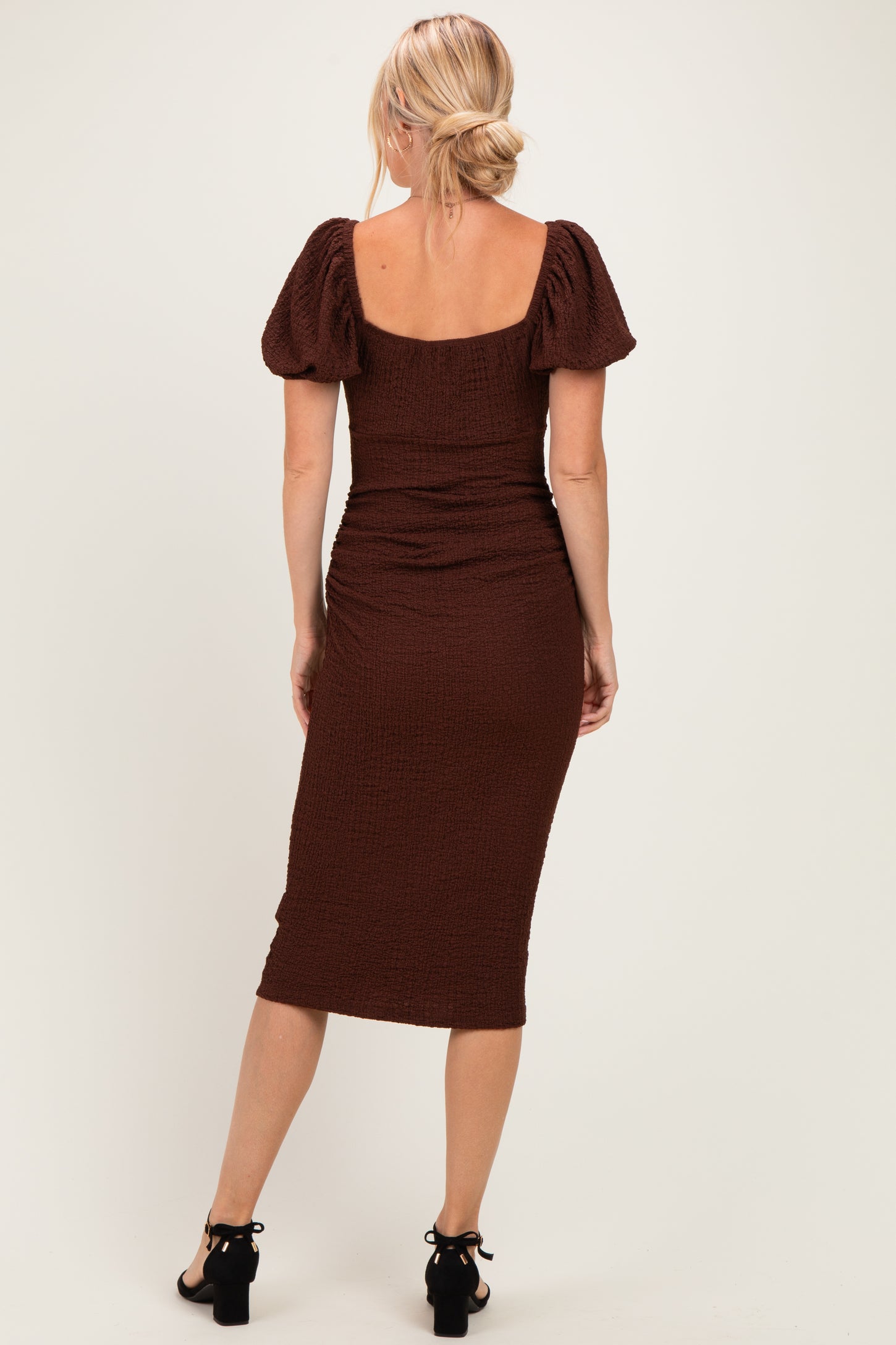 woman wearing a fitted brown midi dress with puff sleeves and ruching detail, shown from the back