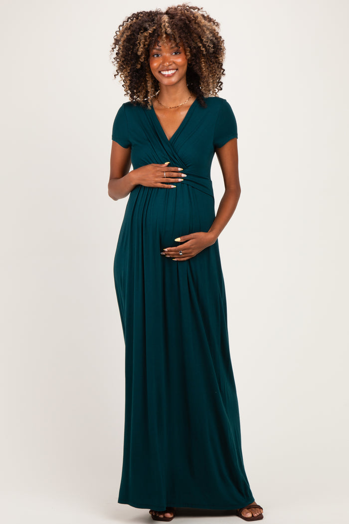 woman wearing a teal maternity maxi dress with a v-neck and short sleeves, holding her baby bump