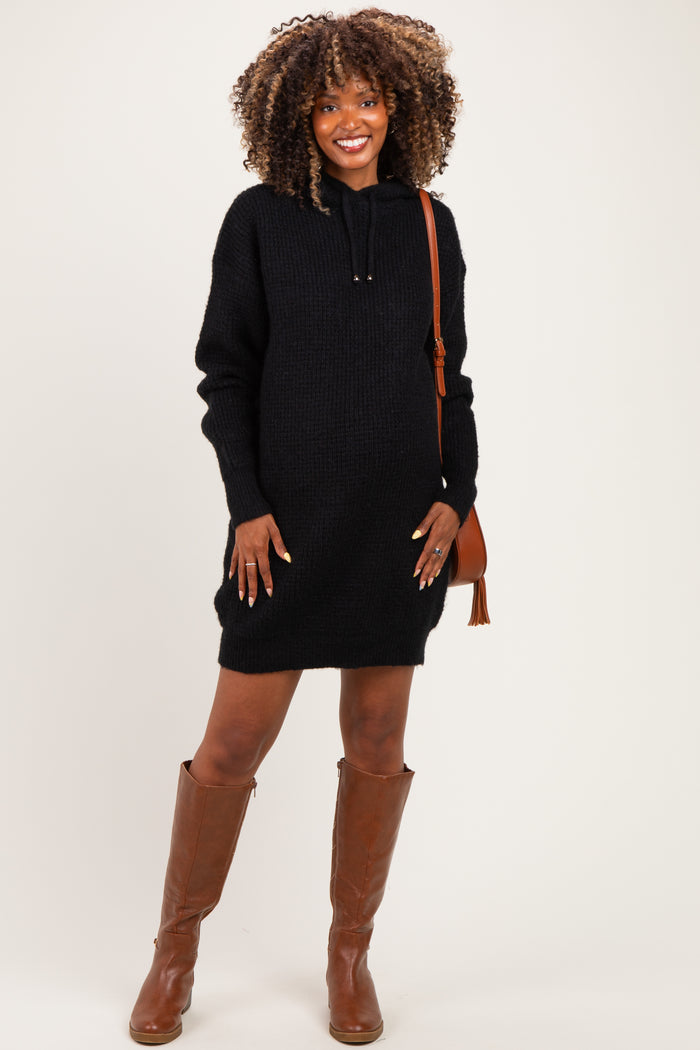 woman wearing a black knitted maternity hoodie dress, showing her baby bump, paired with brown knee-high boots