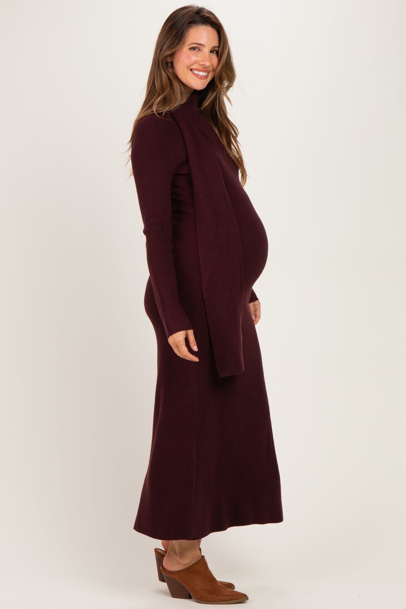 woman wearing a burgundy maternity sweater dress with a fitted silhouette and a side slit, showcasing her baby bump