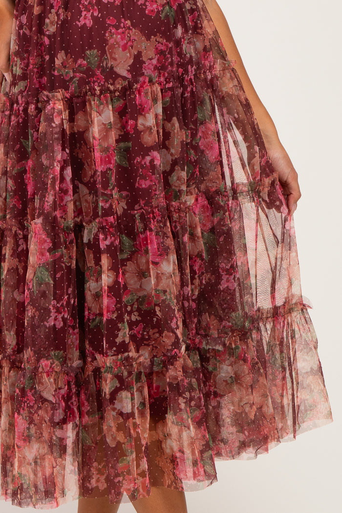 maternity wear in a burgundy floral tiered dress with sheer overlay and ruffles, held by a model