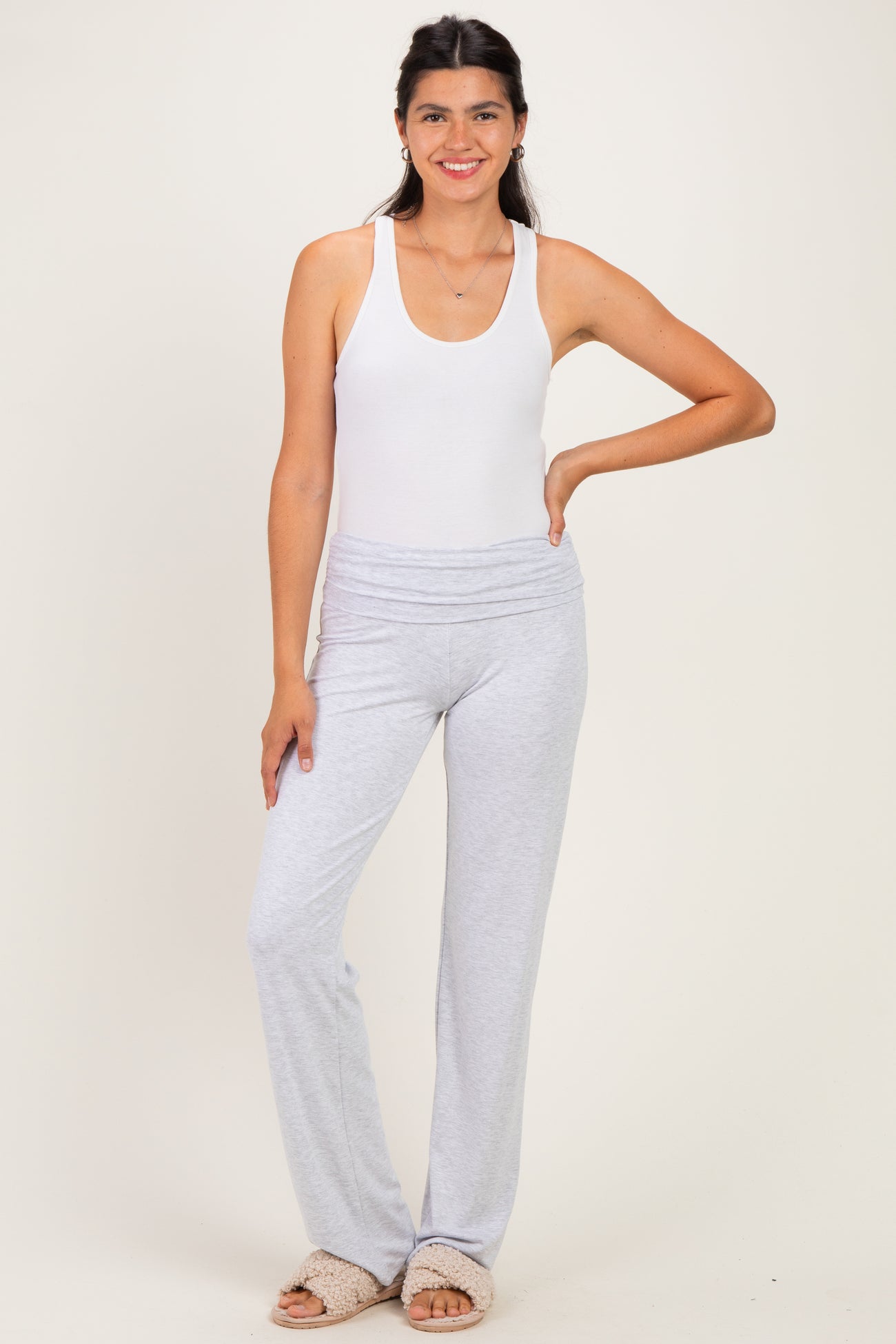 woman wearing a white sleeveless bodysuit and light gray lounge pants, posing with one hand on her hip