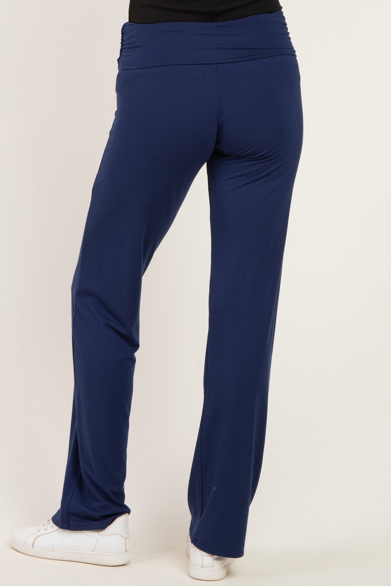 woman wearing navy blue stretchy pants with a foldover waistband and white sneakers seen from the back