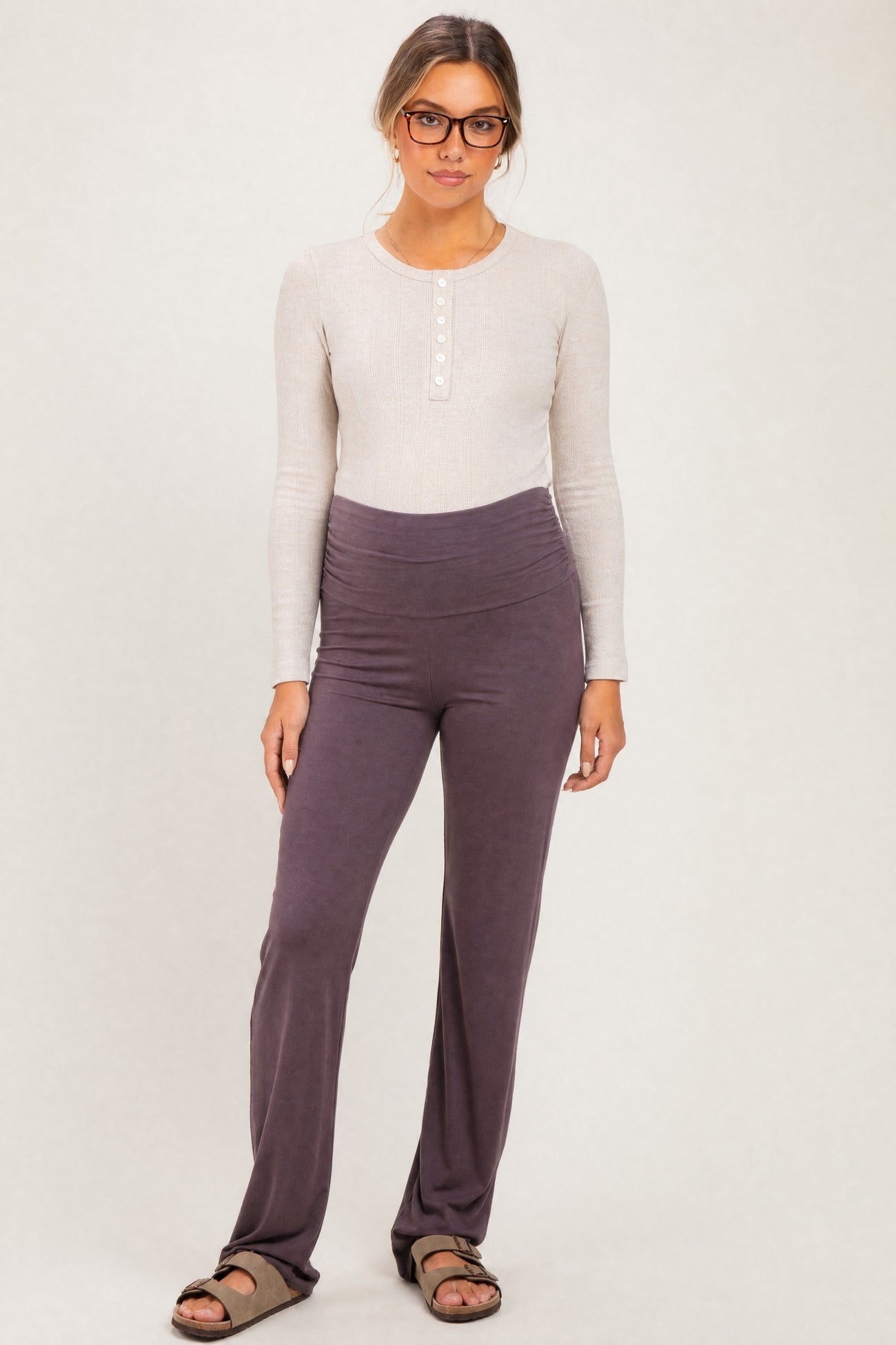woman wearing a light beige long sleeve henley top and dark purple maternity pants with a ruched waistband