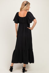 woman wearing a black maxi dress with tiered hem and short flutter sleeves, viewed from the back