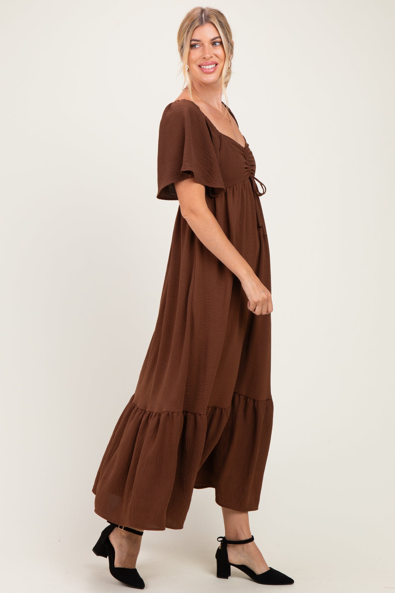 woman wearing a brown maxi dress with short sleeves and a tiered hem, smiling with one hand on her hip