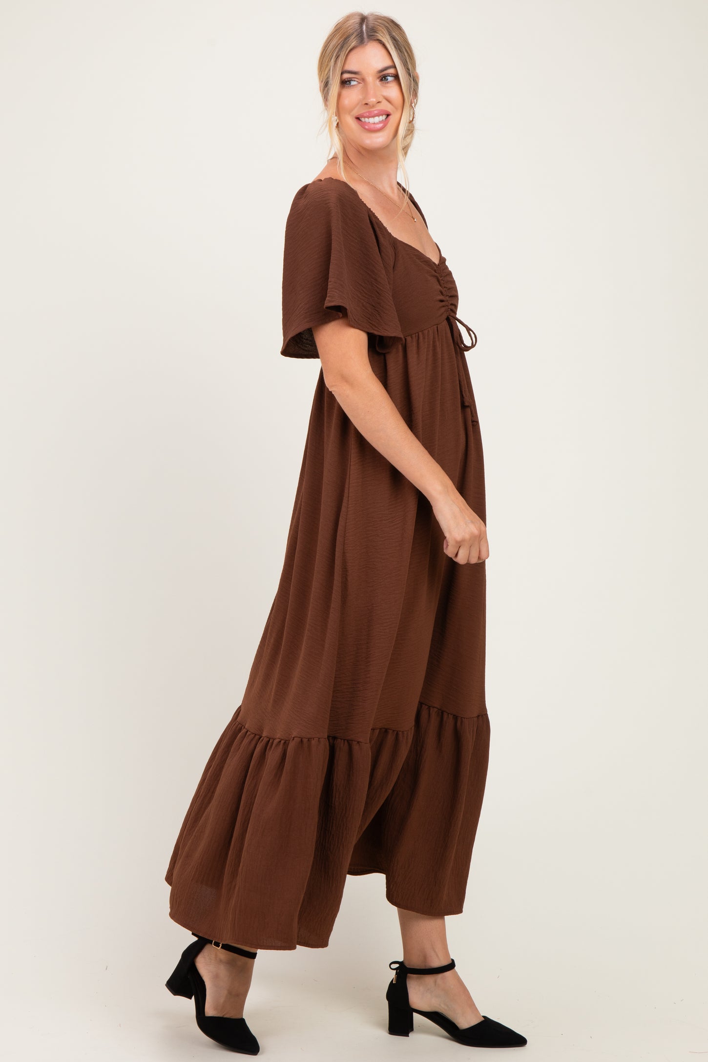 woman wearing a brown maxi dress with short sleeves and a tiered hem, smiling with one hand on her hip